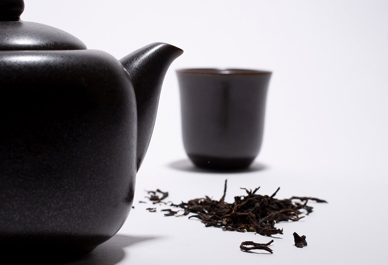 Feuilles de thé fumé du Japon en vrac avec une tasse noire et une théière noire.