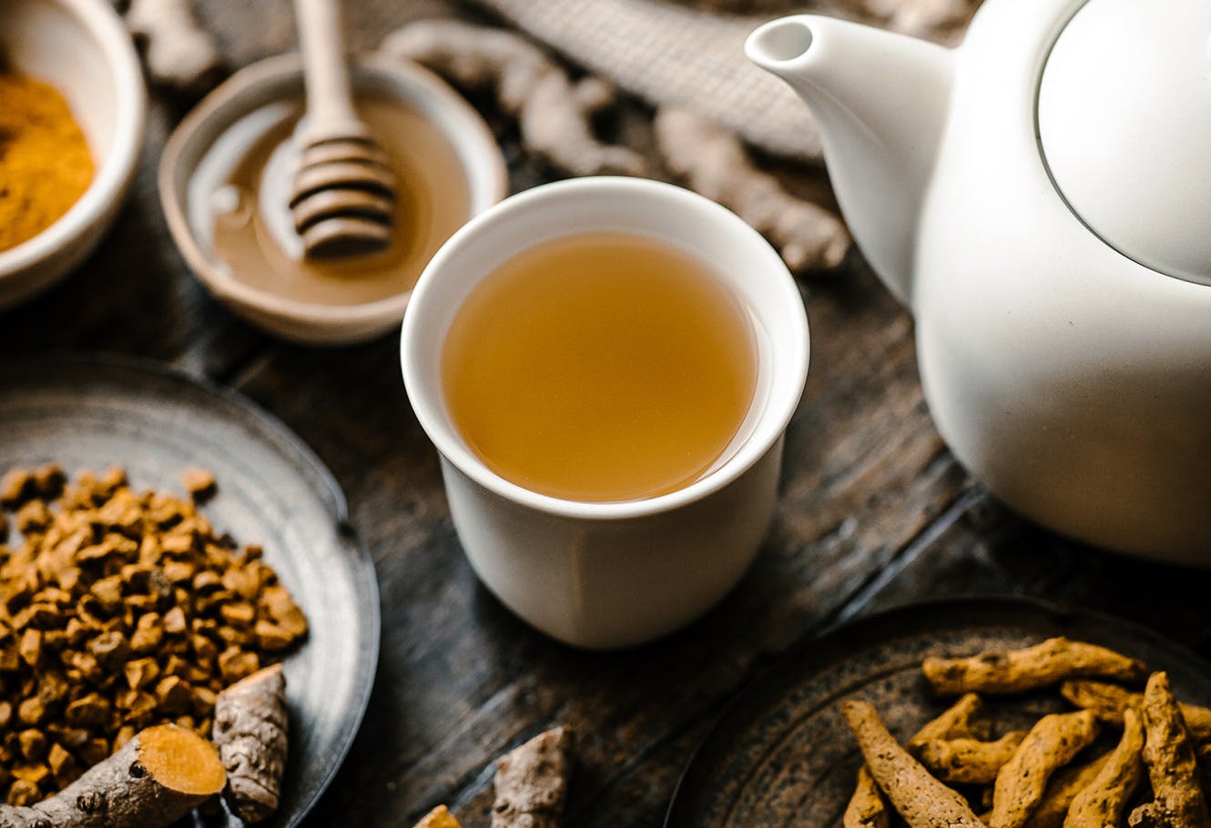 Tasse de thé contenant une infusion de curcuma, racine de curcuma et cuillère de miel sur une table.