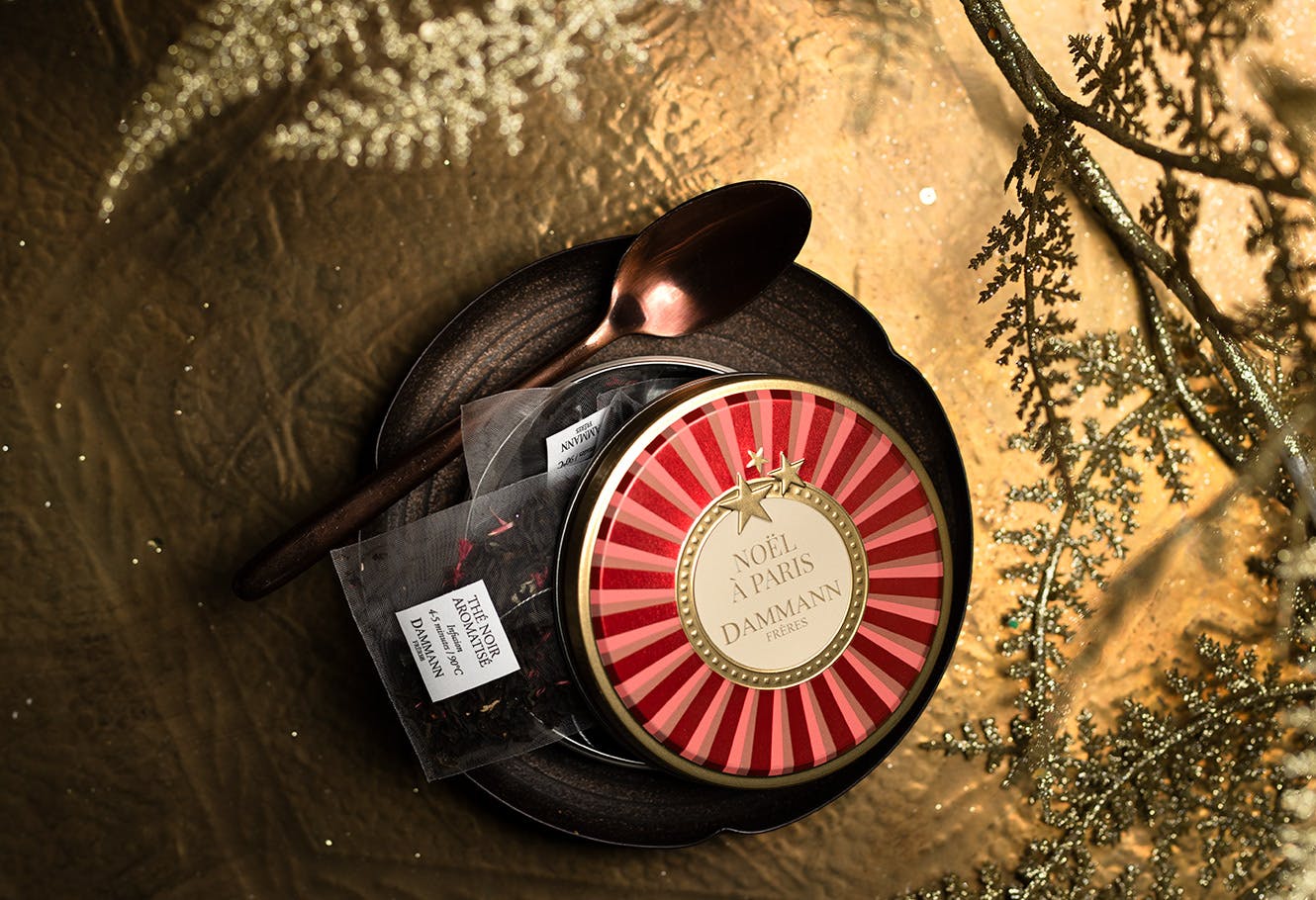 Boîte ronde de sachets de thé "Noël à Paris", finition métal, posée sur une sous-tasse et sa petite cuillère.