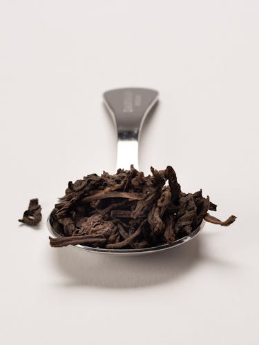 Stainless steel measuring spoon with dark tea in bulk.