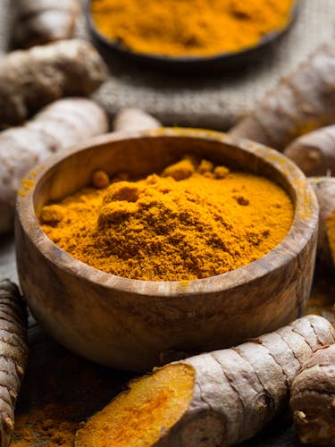 Turmeric powder in a bowl and chopped turmeric root.