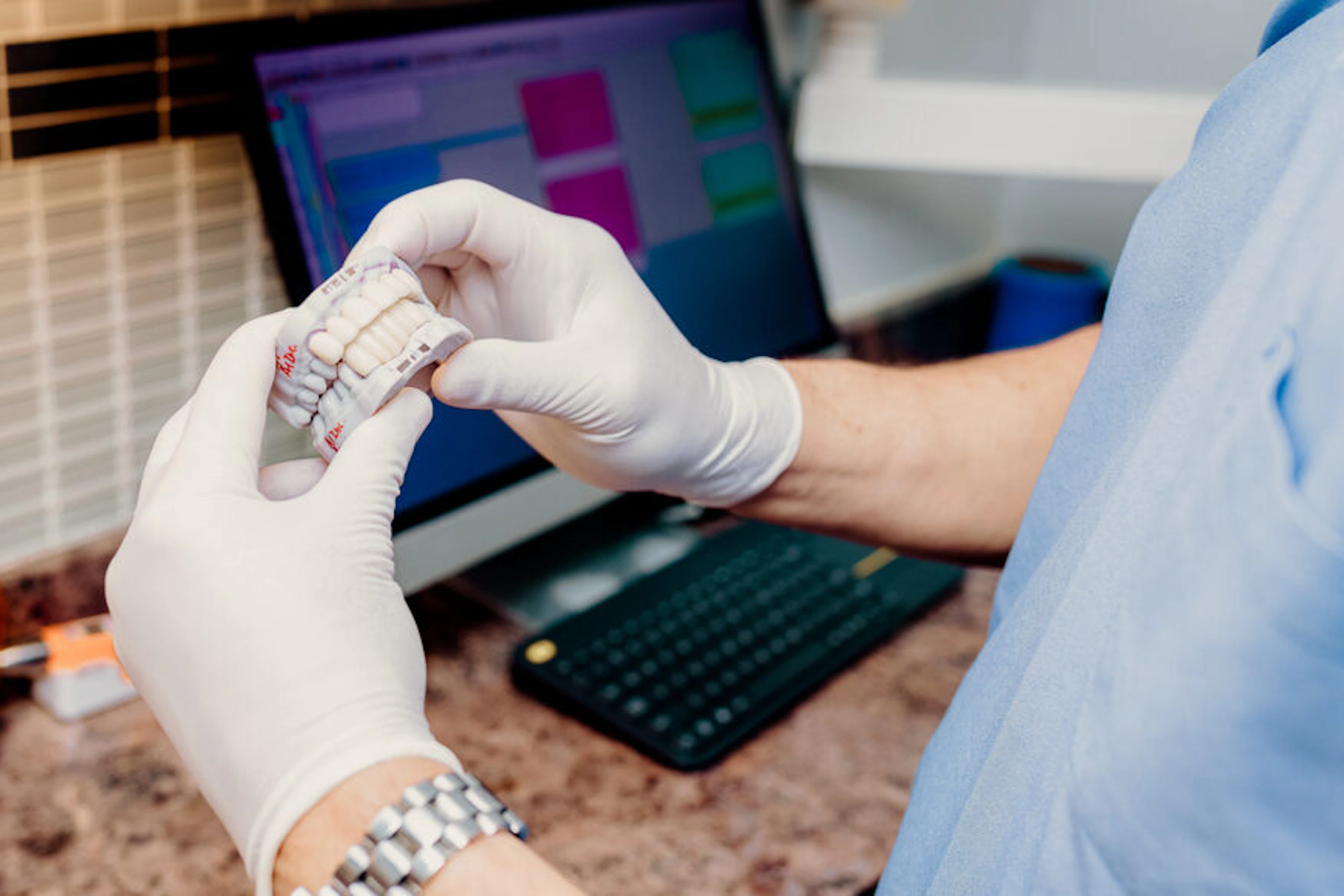 Dental lab technician holding a dental restoration model next to a computer monitor showing scan software