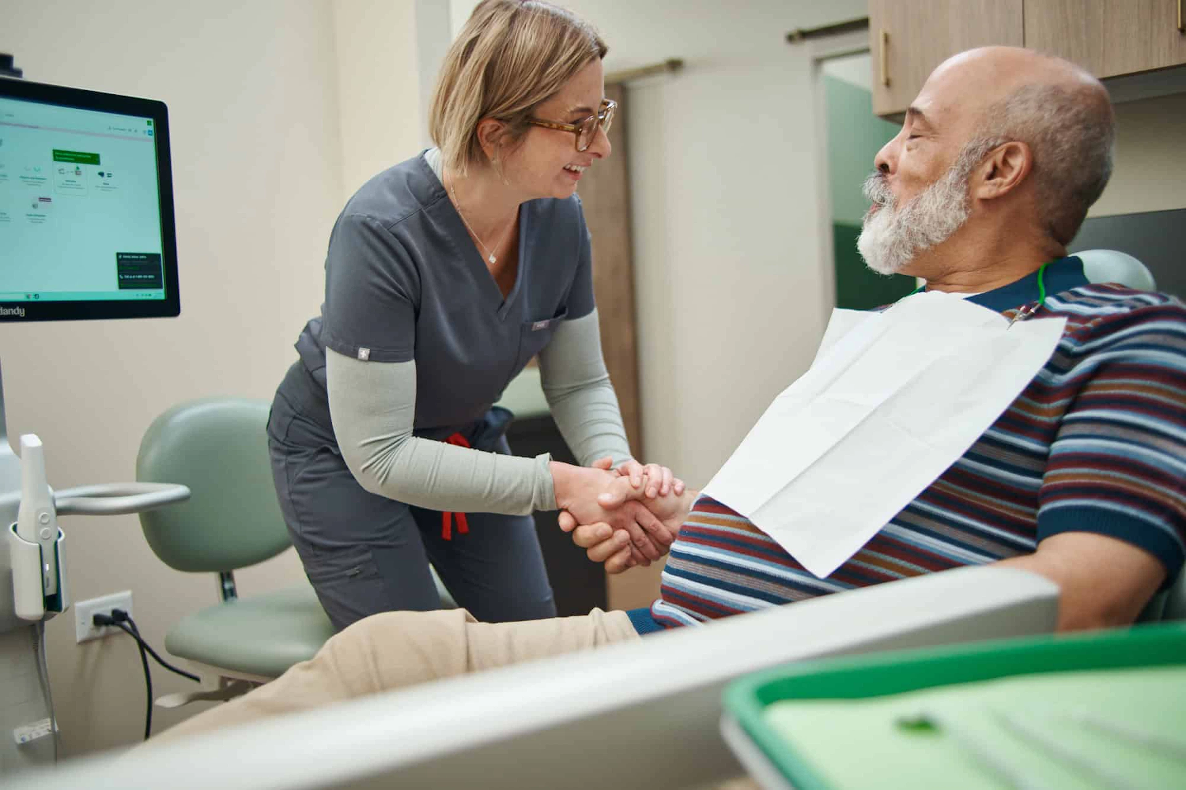 Dentist shaking hands with a smiling patient in the dental chair