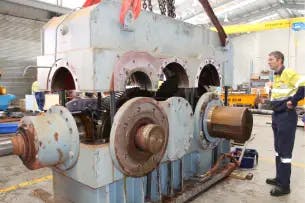 Engineer inspecting a large industrial gearbox with exposed shafts and gears during a bearing failure analysis to identify damage and root causes.