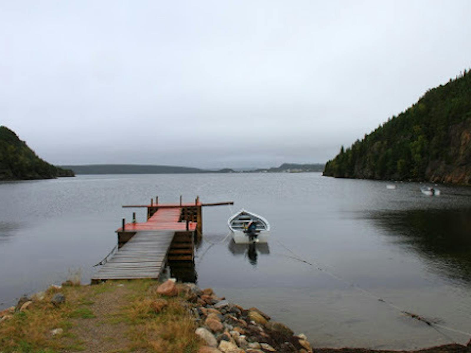 une scène d'un lac avec un quai à moitié peint en rouge au milieu s'étendant dans l'eau. Un bateau est attaché au quai et entouré de montagnes.