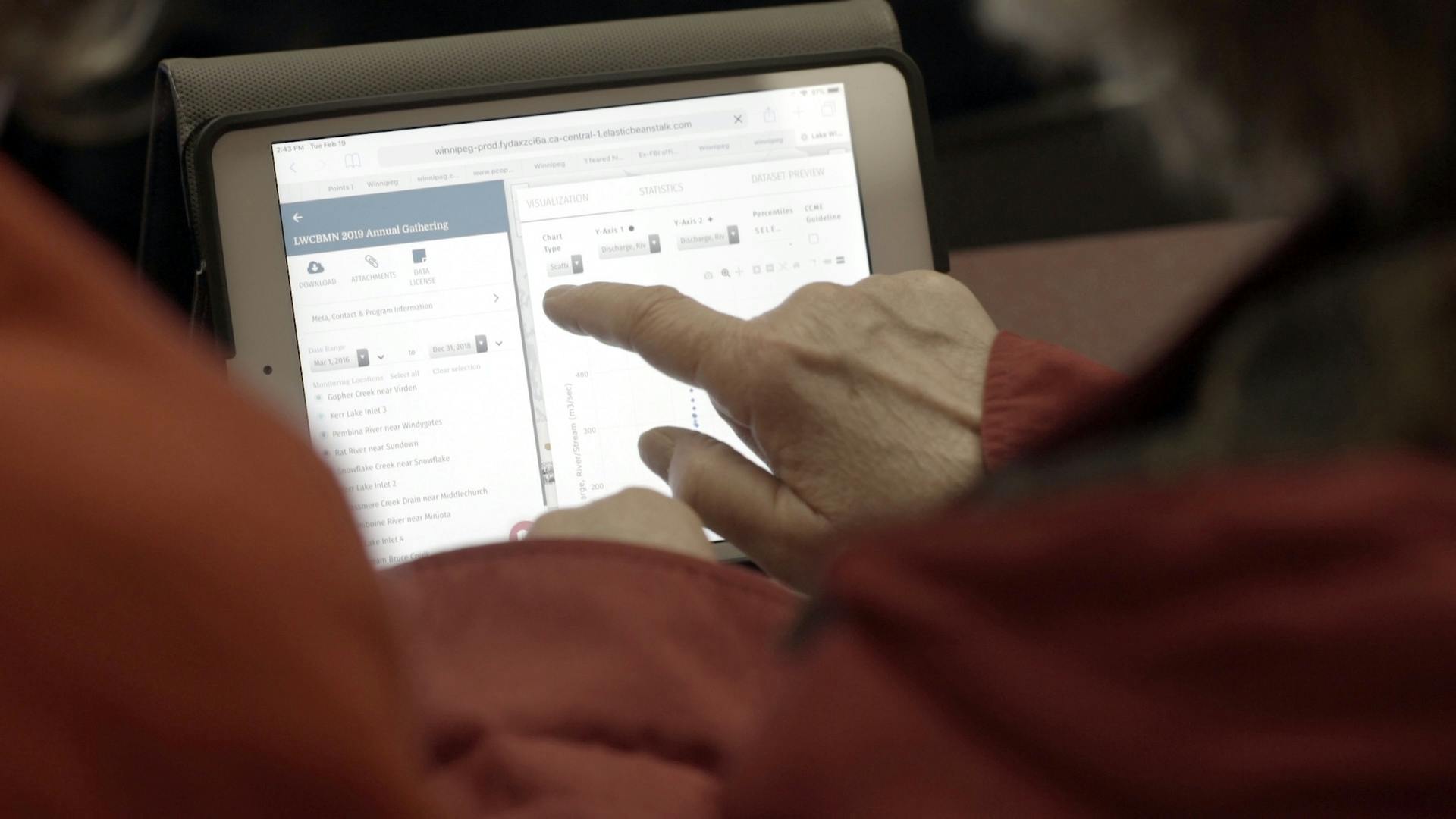 hand of an elderly person pointing at a tablet displaying a datastream visualization page