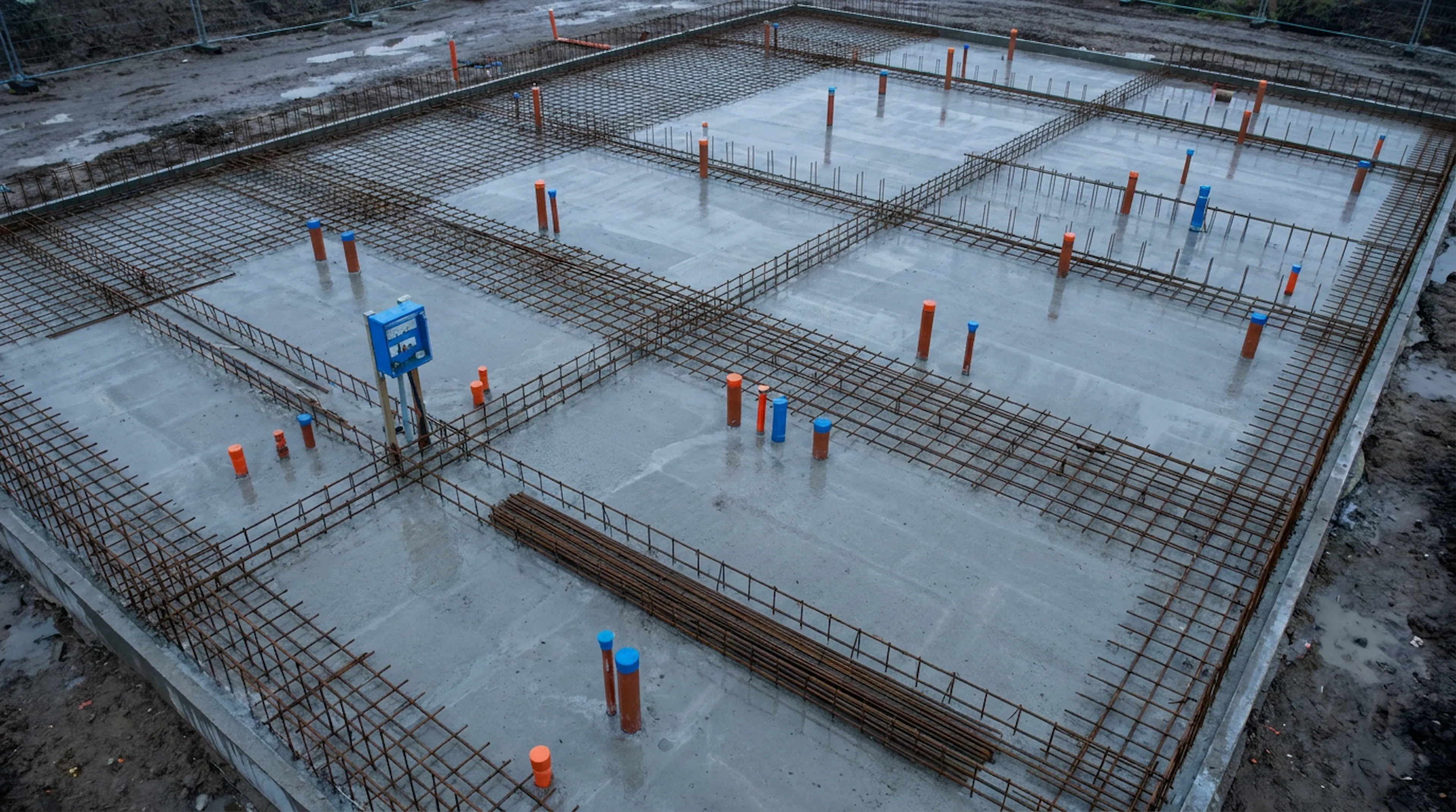 A freshly poured concrete foundation slab with rebar and conduit laid out precisely, before any building exists on it