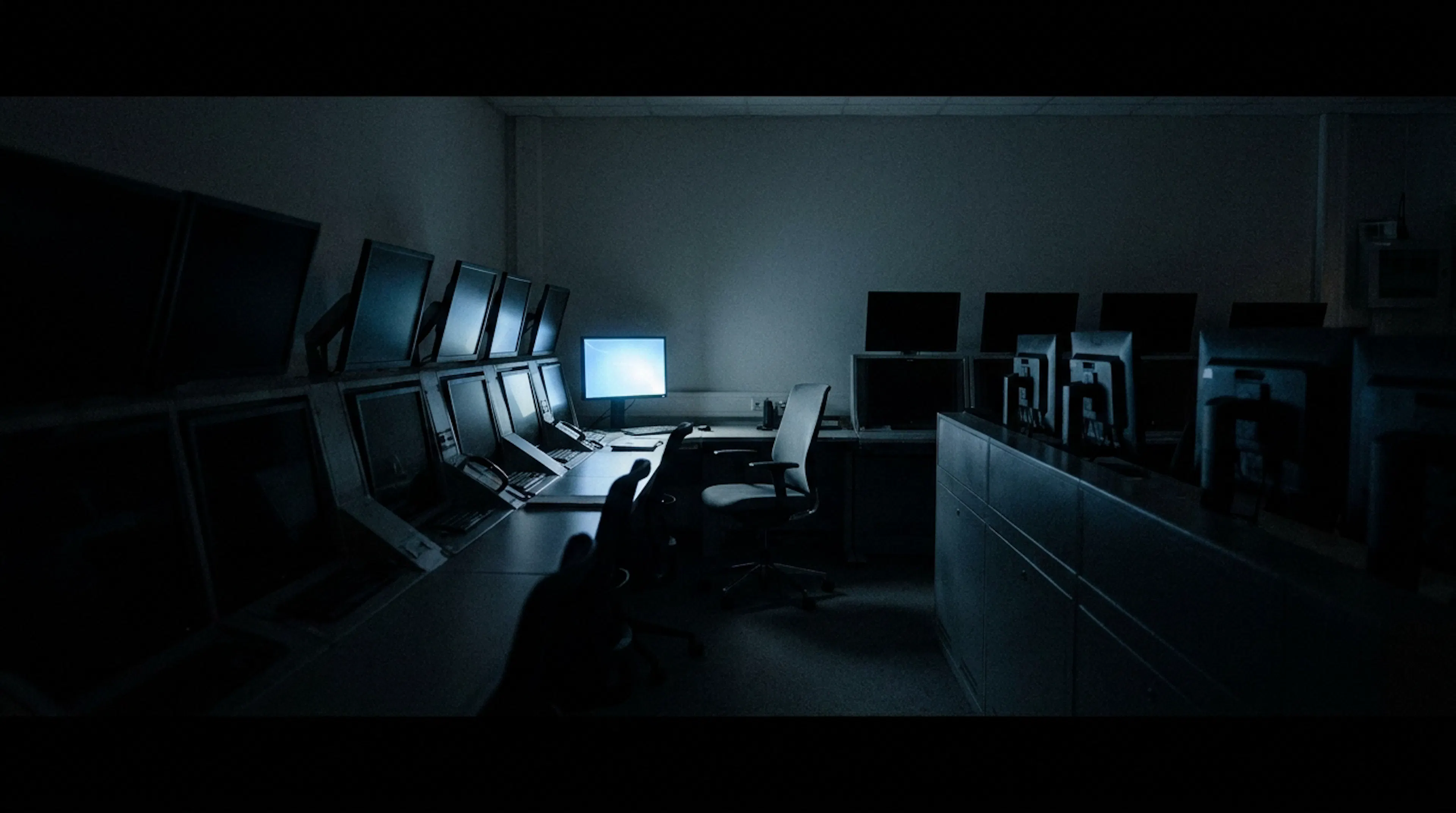 A darkened operations room after hours with one monitor still glowing over an empty chair