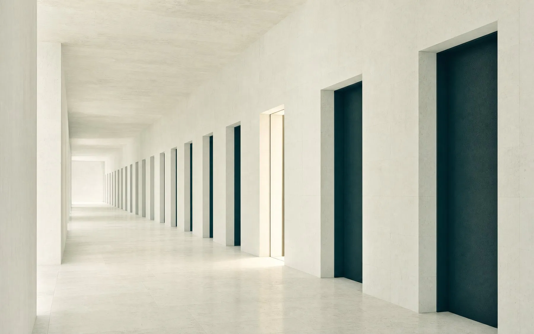 A long limestone corridor of identical closed doorways, with one partway down standing open and lit
