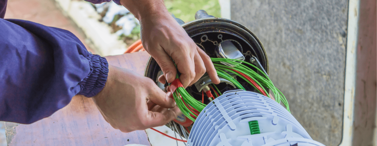 Hands of a fiber optic technician repairing an equipment with green and red cables for proper fiber networks
