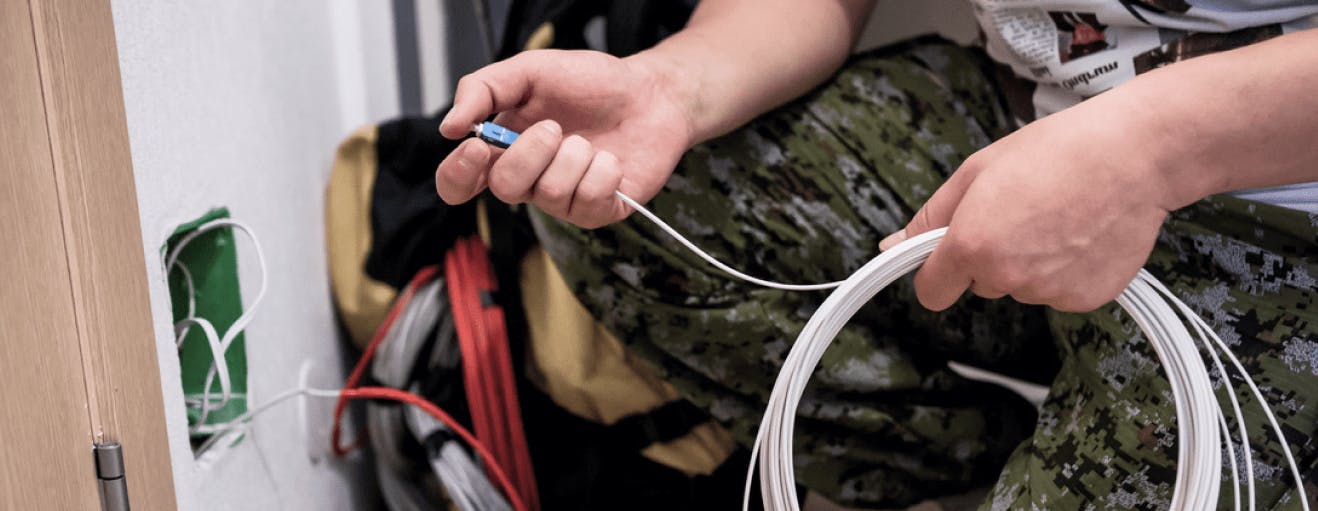 Trabajador de campo instalando fibra óptica con cable blanco a una pared con un socket verde