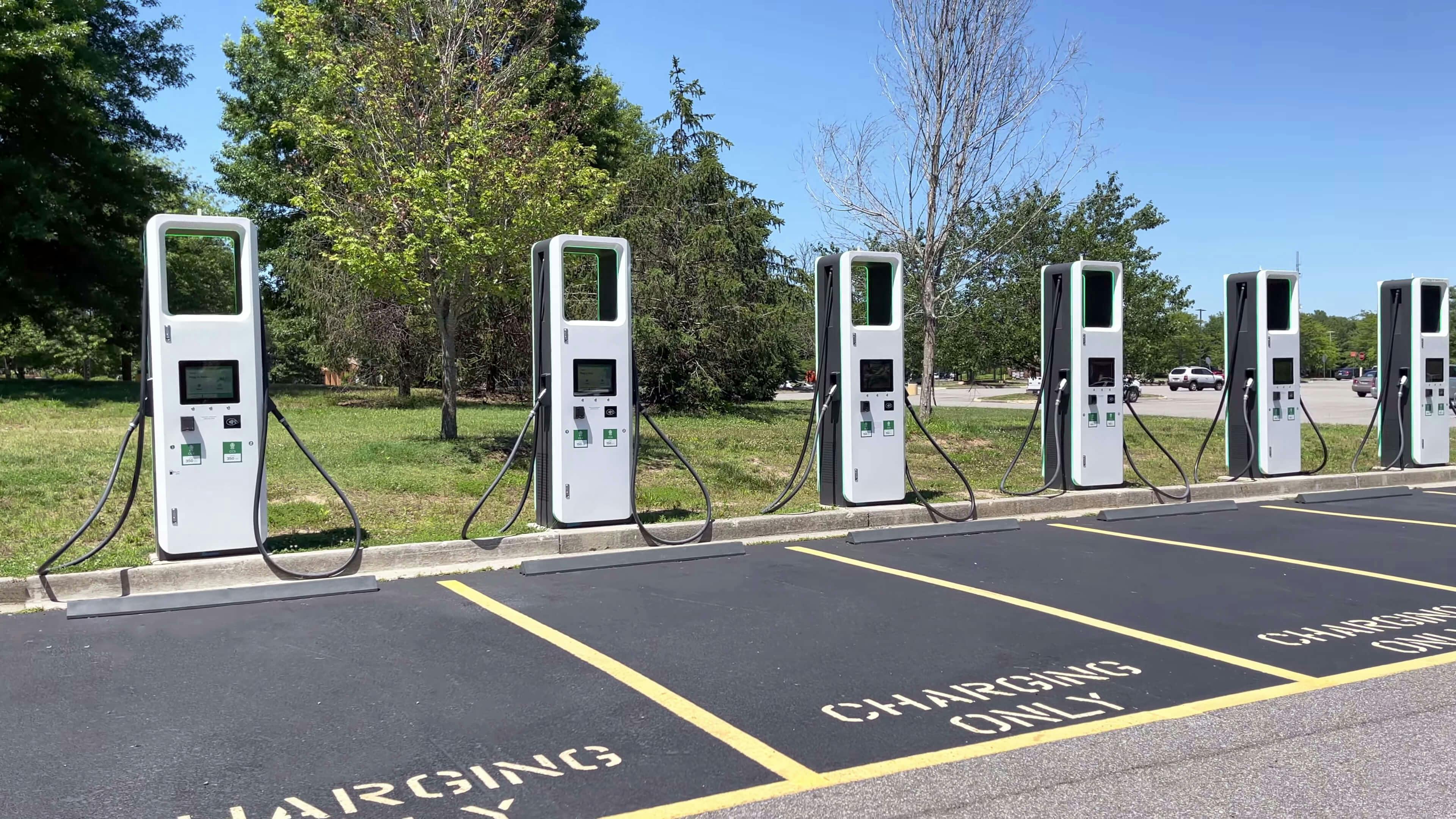Seis cargadores blancos para vehículos eléctricos perfectamente alineados en una plaza de aparcamiento.