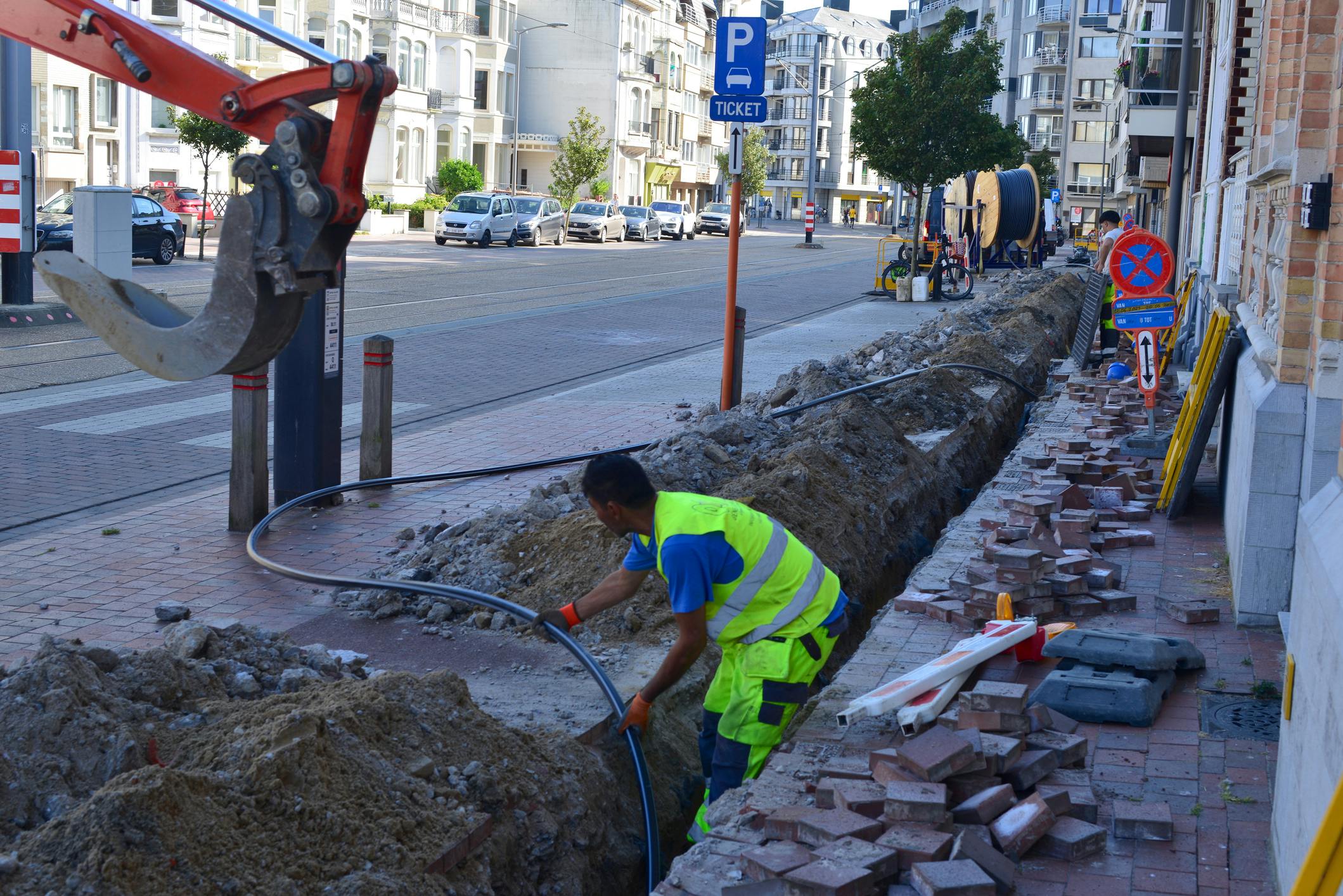 Technician installing fiber on a pre-dug street for network deployment in Belgium.