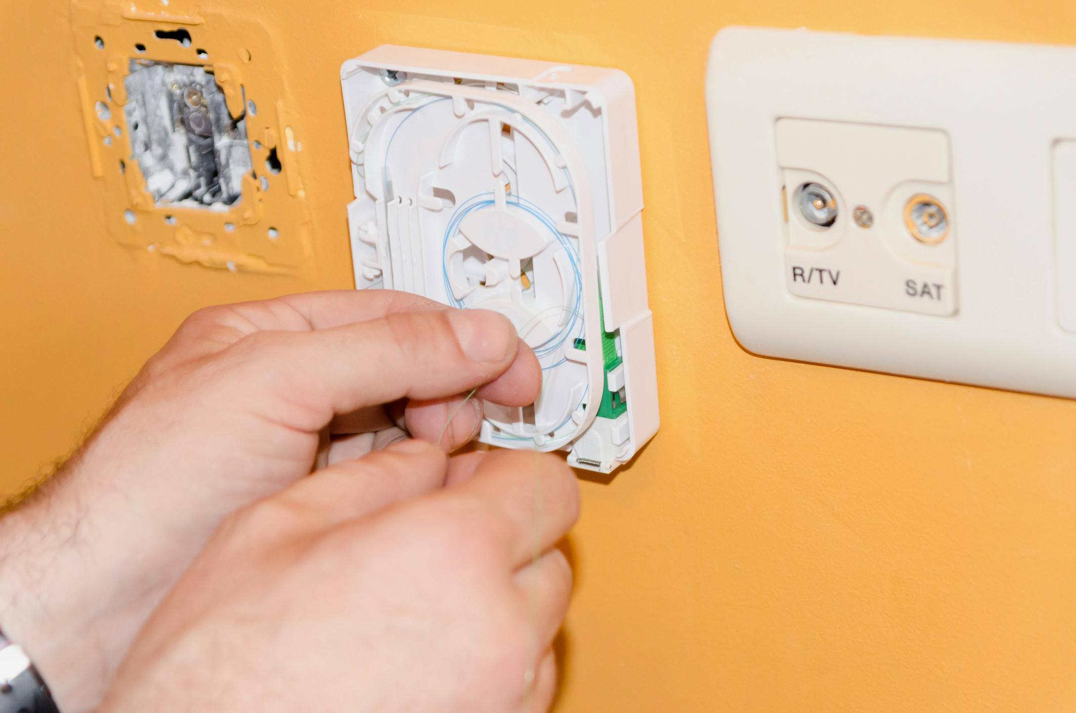 A field technician connecting a termination point with fiber optic cables on a yellow wall