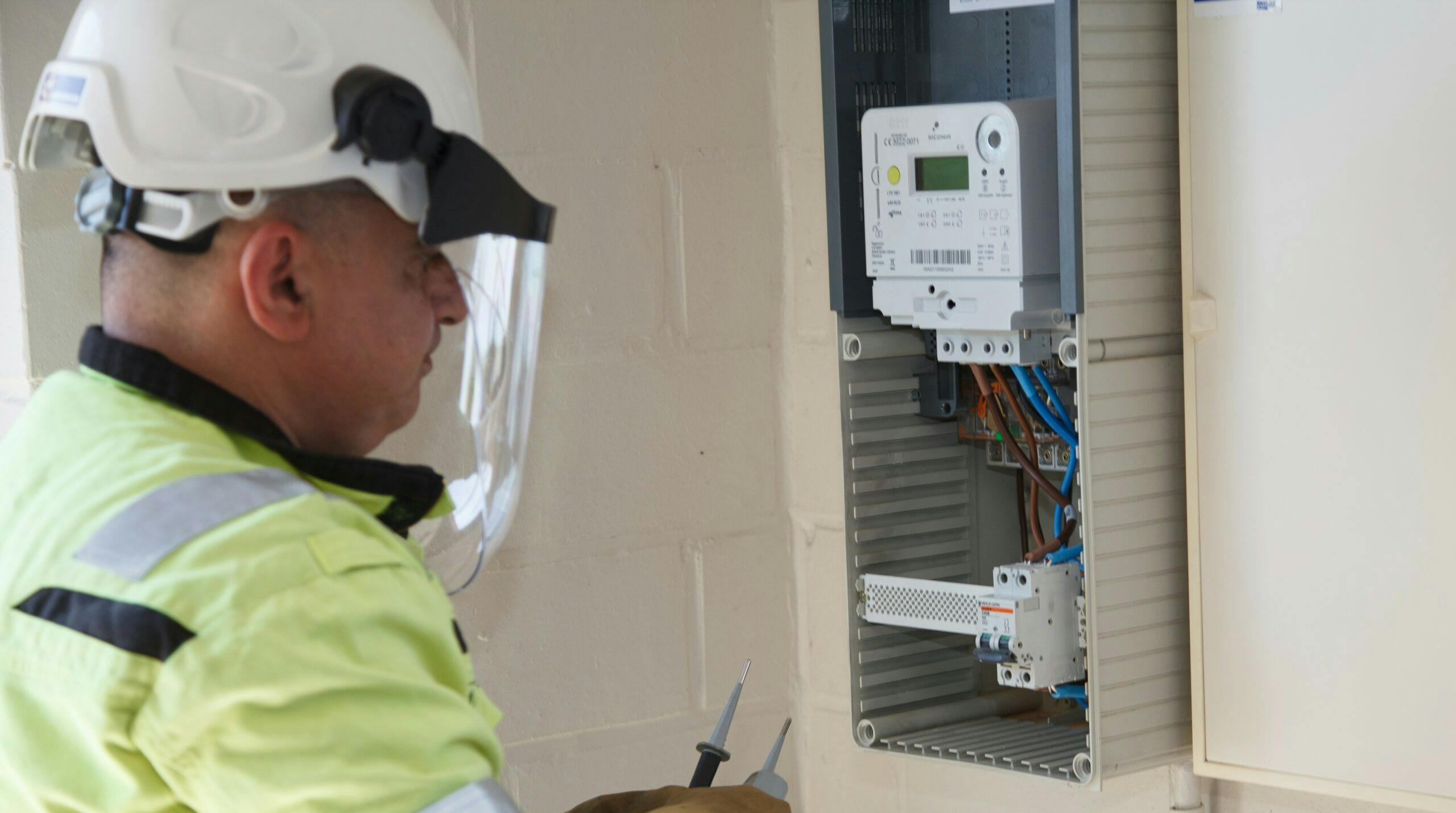 Unit-T technician in a yellow vest and with a white construction helm repairing a smart meter