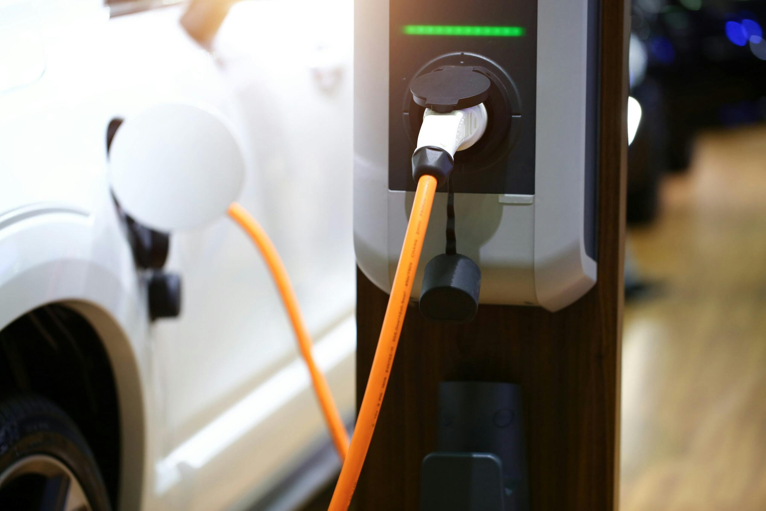 White car using a black EV charging point with an orange cable