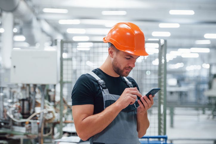 Technician wearing an orange helmet and using his smartphone