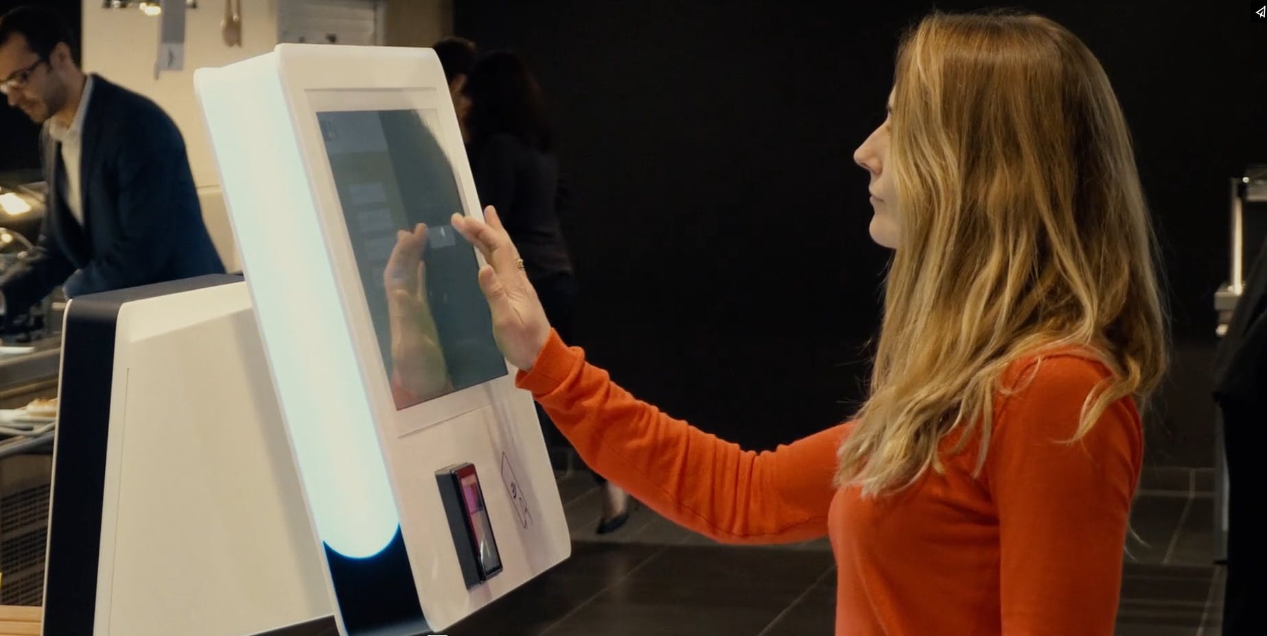 Mujer tomando pasando una orden de comida en una caja de libre servicio integrada con Computer Vision