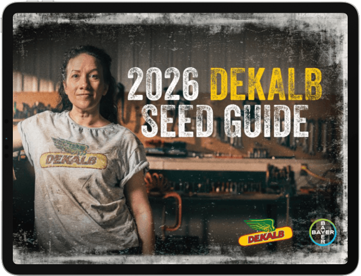 A woman in a DEKALB t-shirt stands in front of a workshop. Text reads "2026 DEKALB SEED GUIDE," with DEKALB and Bayer logos at the bottom right