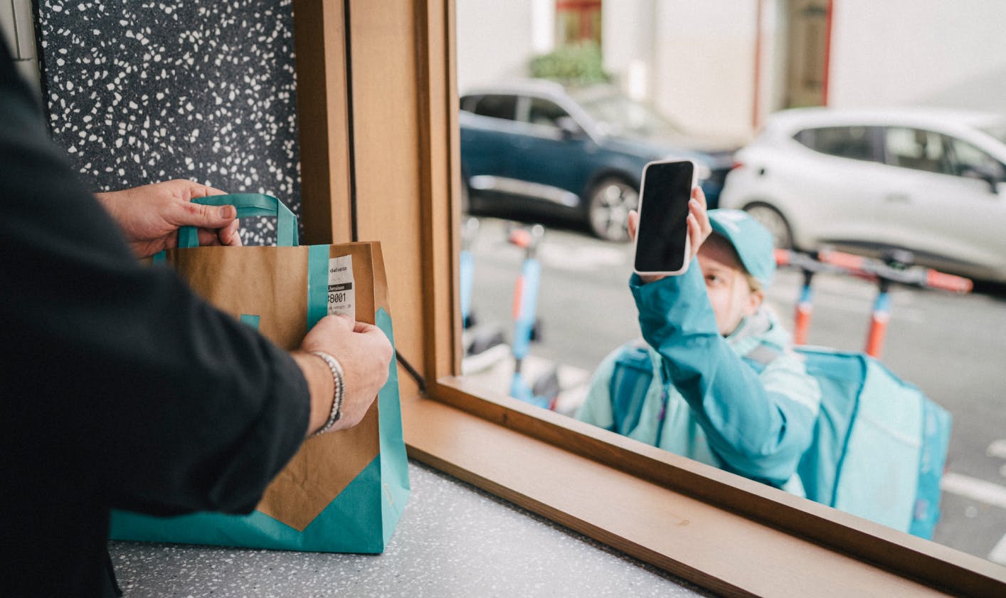 A female Deliveroo rider showing restaurant staff a pick up code on their mobile