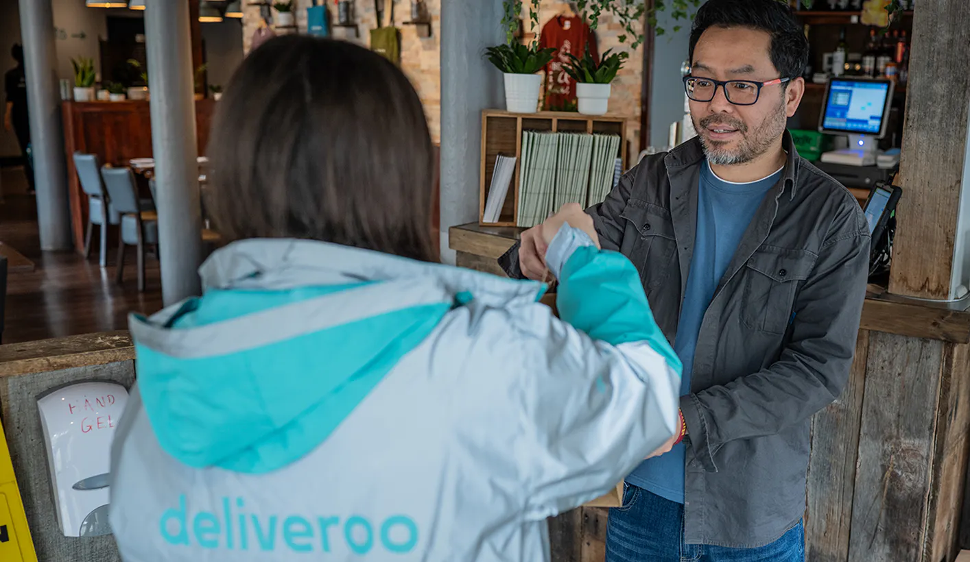 Restaurant staff handing over an order to a Deliveroo rider