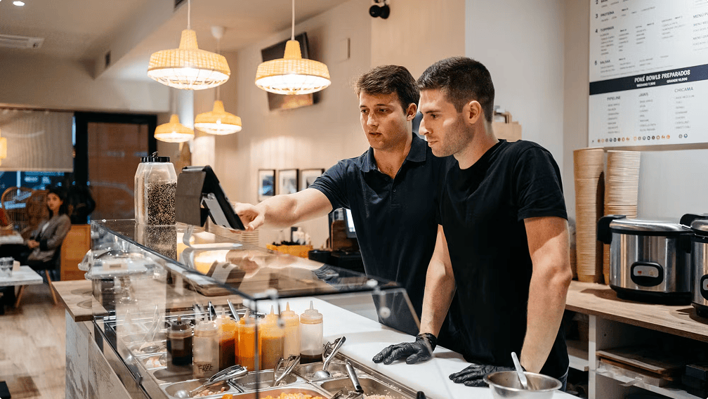 Two restaurant staff working behind the counter, preparing food and managing orders for Deliveroo customers.