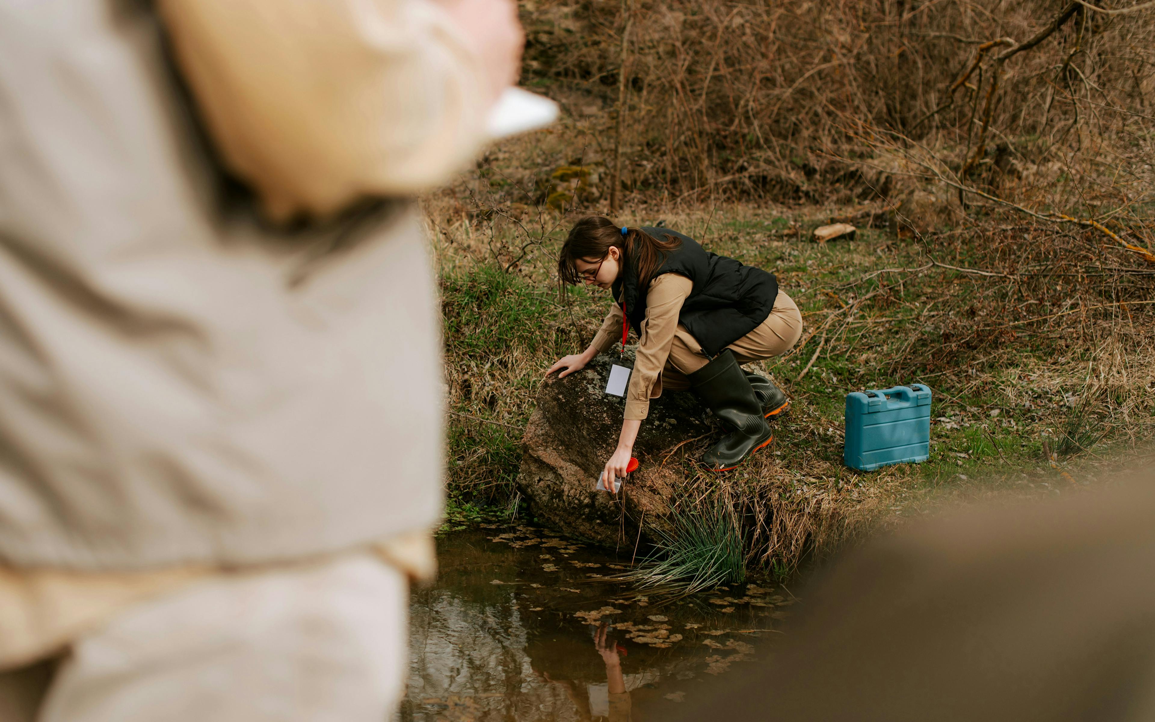 Woman crouching down to take a sample from a river.