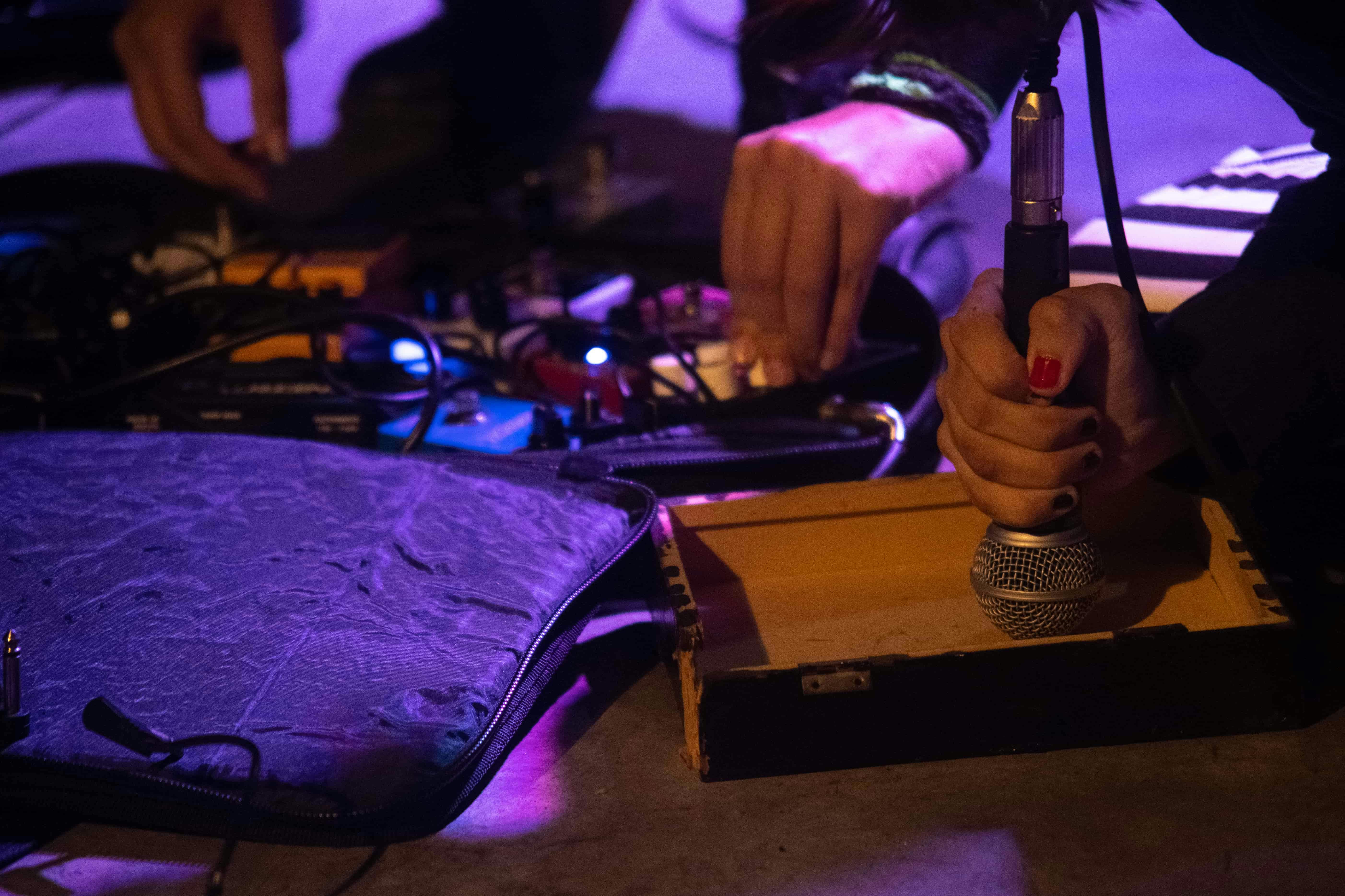 mãos manejando pedais de guitarra e um microfone dentro de uma caixa