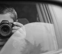 Homem dentro de um carro com vidro aberto pela metade fotografando
