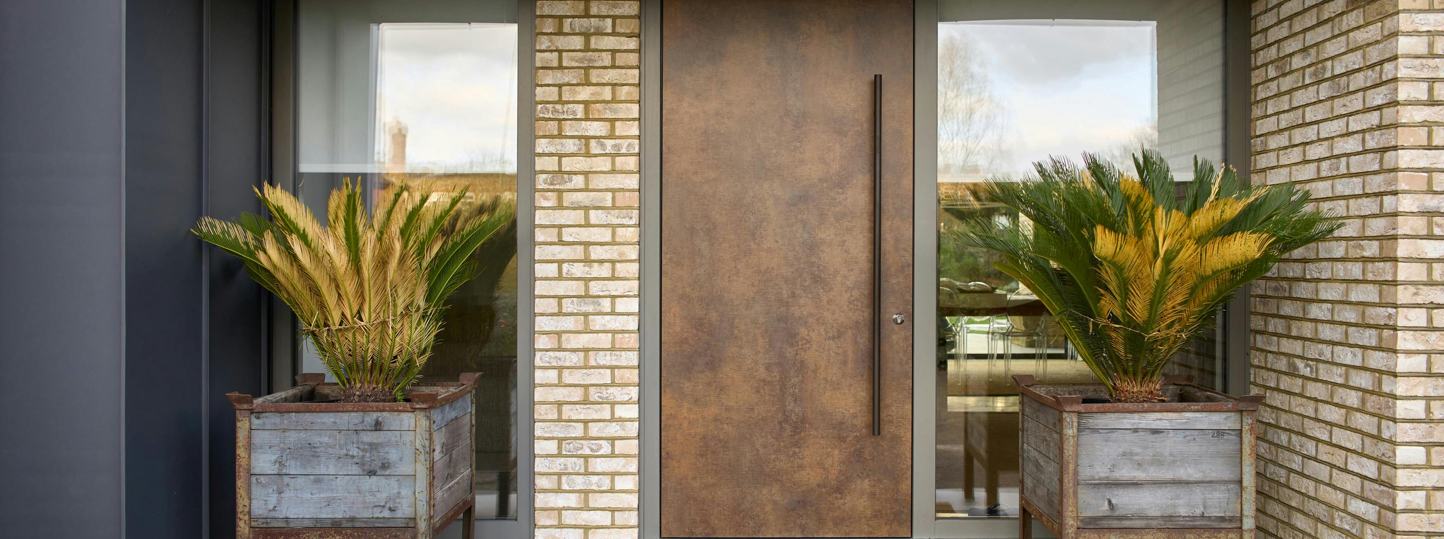 Modern home entrance with a luxury front door by Deuren. A slab style, the Olivio door has a warm patina bronze, metallic finish