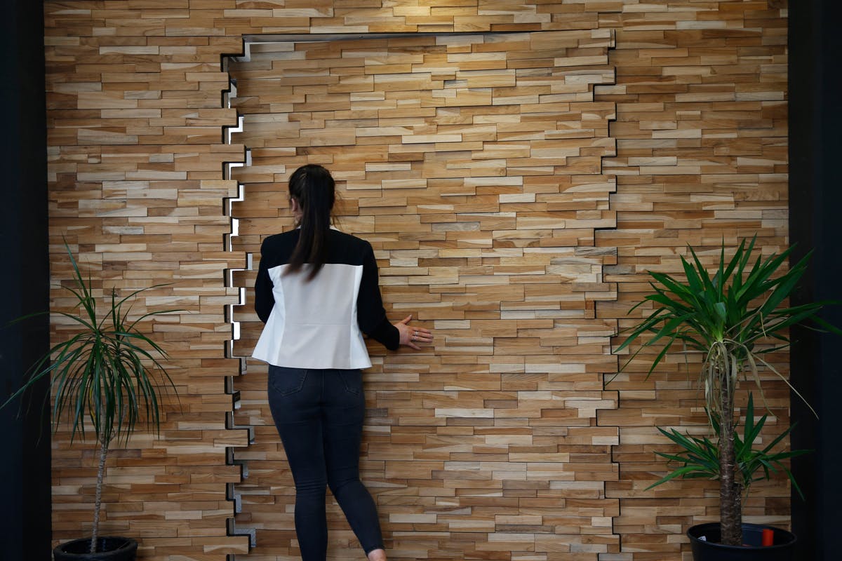 Woman going through bespoke and contemporary secret pivot door by Deuren. The door and surrounding wall surfaces are finished in stacked timber blocks. A creative door style.