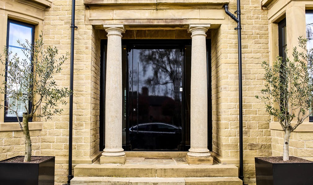 large bespoke glossy black front door behind two pillars