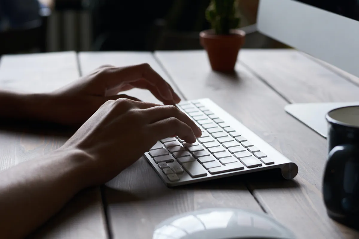 Hands typing on a keyboard at a comptuer.