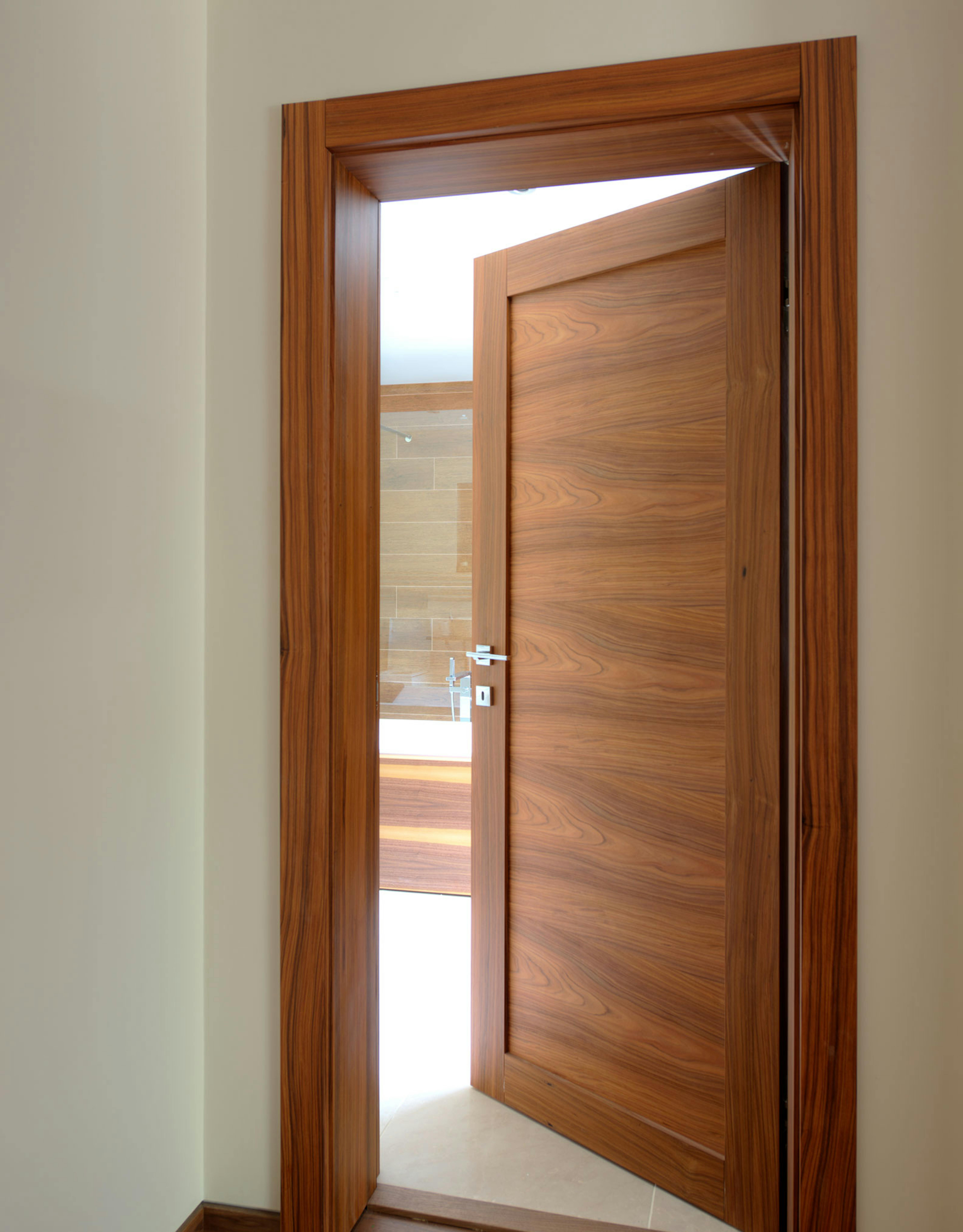 Contemporary pre-hung door set in Trem H, Rosewood finish, by Deuren. Door ajar with glimpse of bathroom.