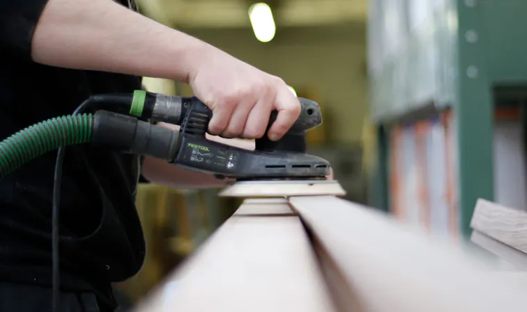 Close-up of someone using a power sander to smooth a piece of wood.