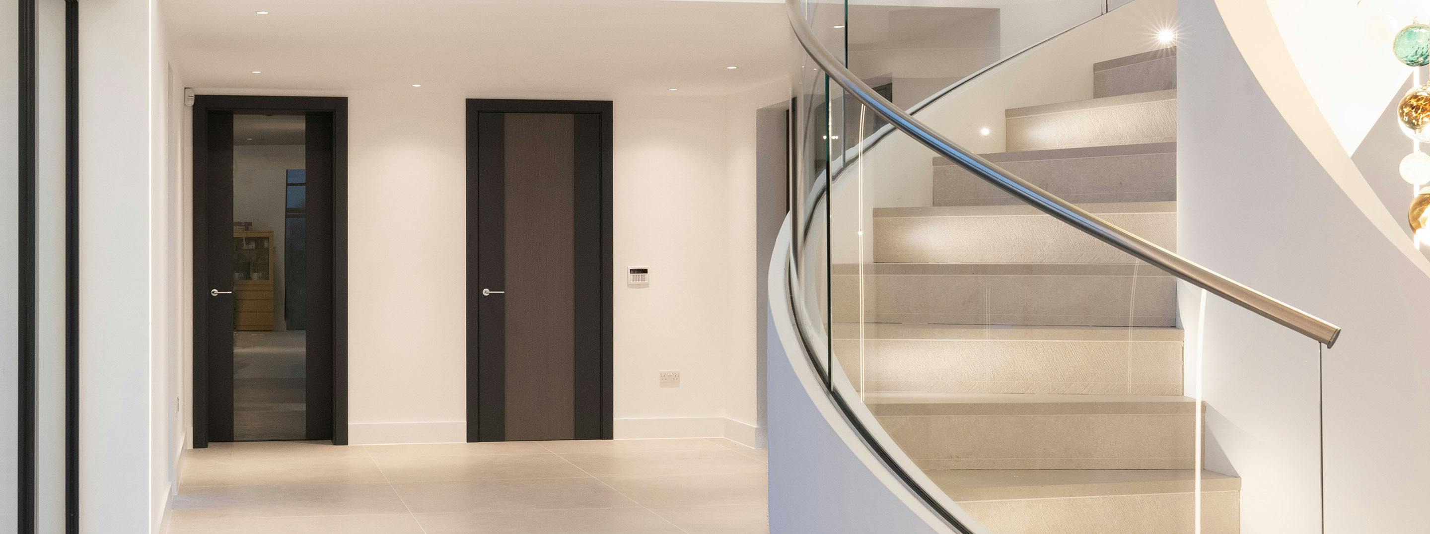 Contemporary hallway and spiral staircase, with two Deuren made-to-measure internal doors - styles include Linea and Trem Glazed in a dark grey painted finish.