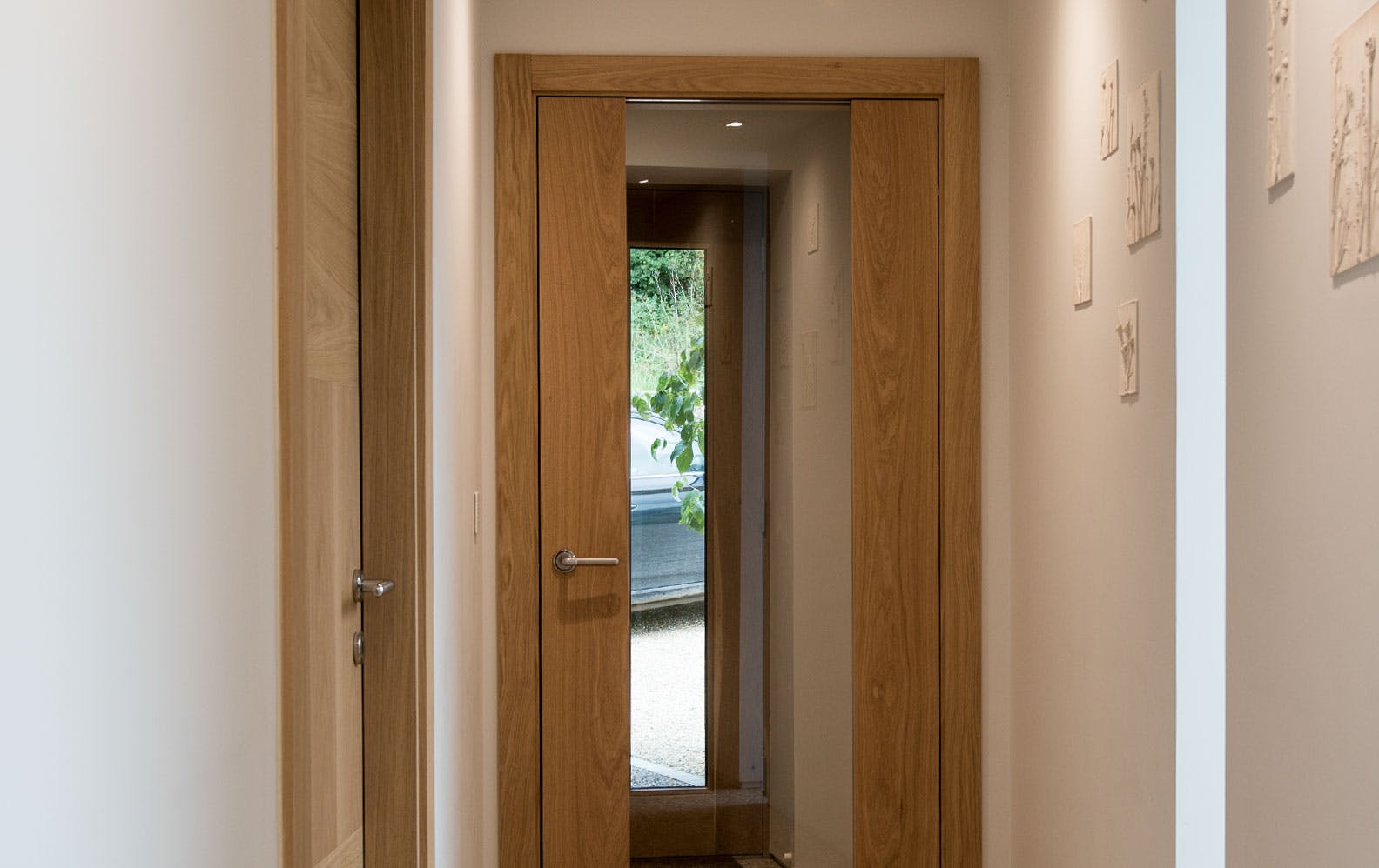 Hallway corridoor featuring a pre-hung Deuren door set. Style is Trem glazed, a full height pane of clear glass held between two full height strips of natural oak veneered timber. 
