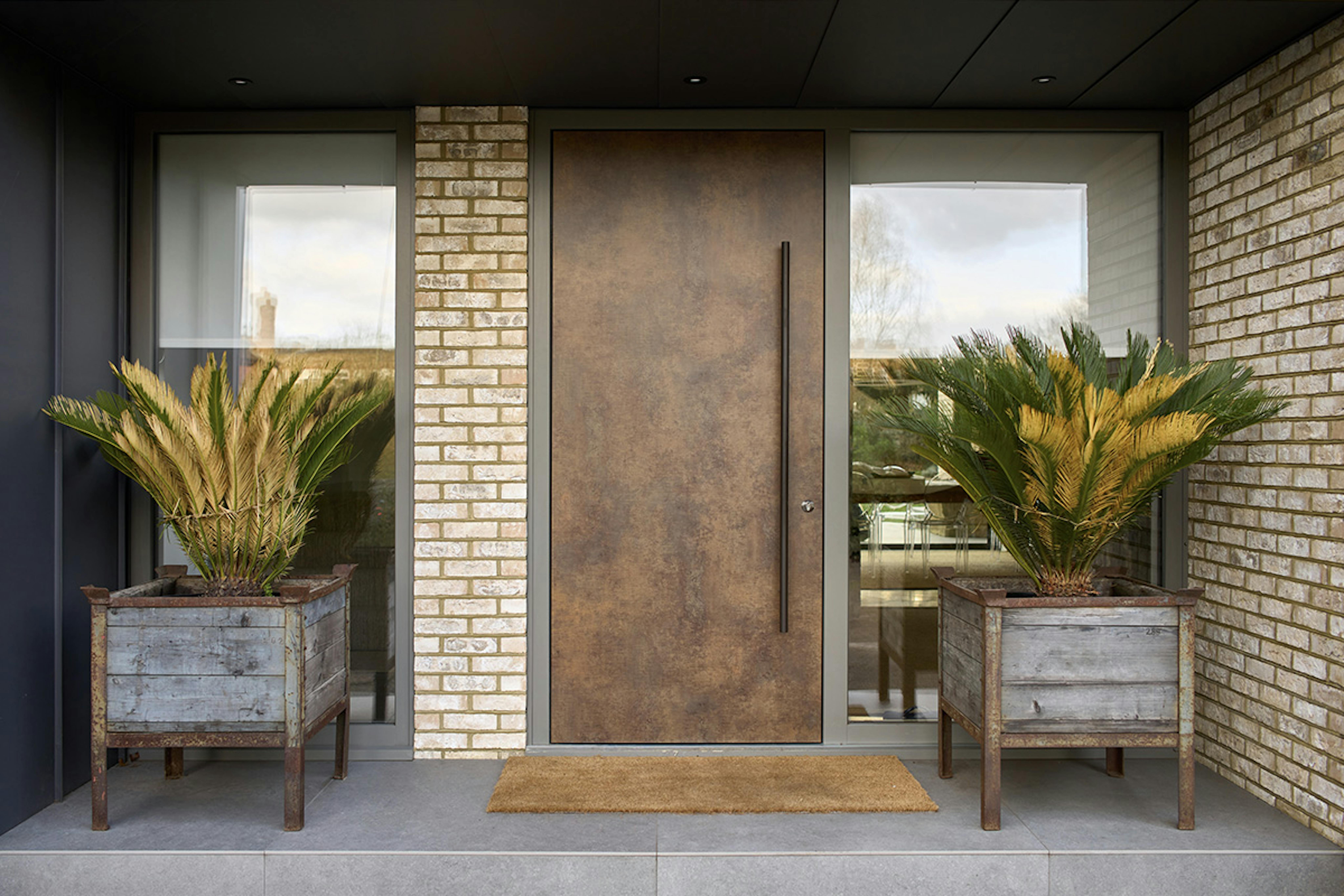 Modern front door by Deuren. A slab style, the Olivio door has a warm patina bronze, metallic finish. with a full height wide window to the right side.