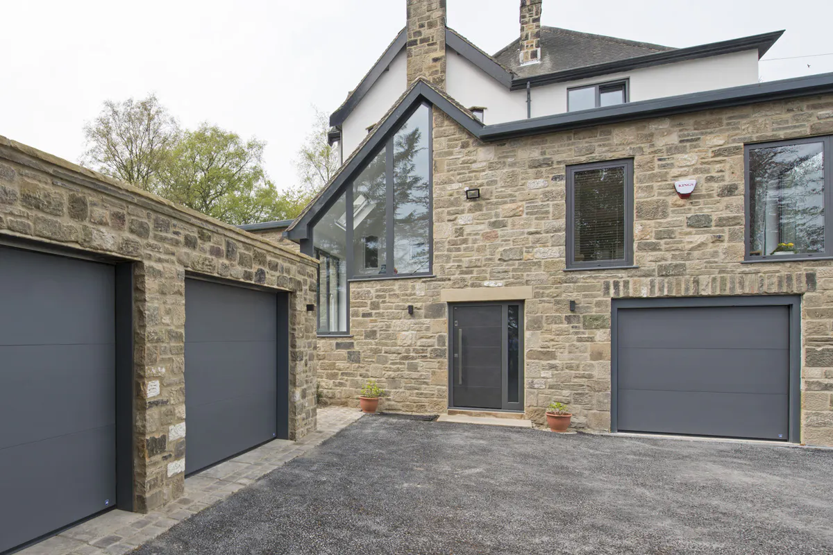 stone home exterior featuring three matching garage doors and a closely matched front door style. Pianura 1, mid-grey paint finish.