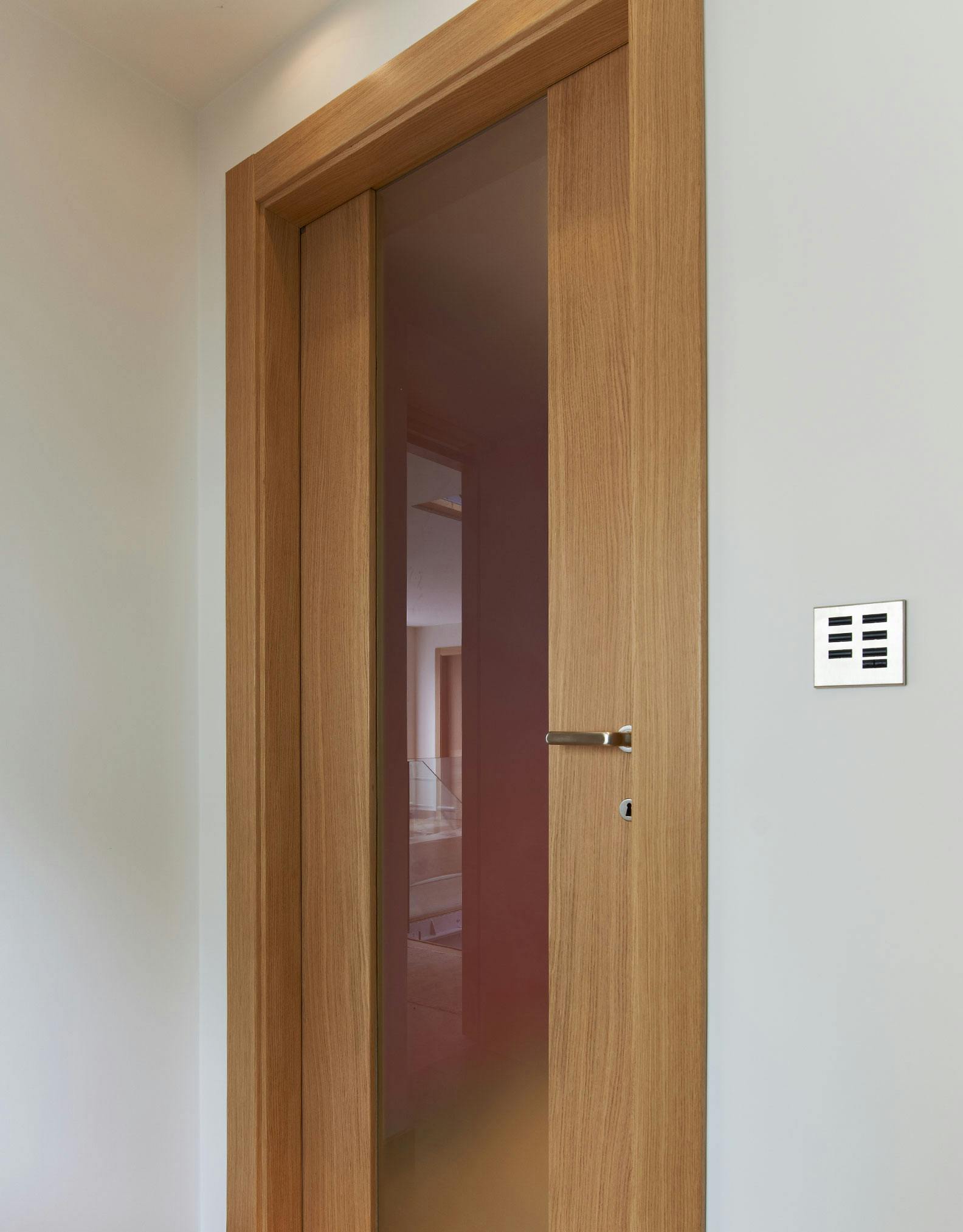 A modern, single leaf, internal door set by Deuren - Trem V glazed style, Natural Oak finish. Full height, satin glass central section with timber strips to both sides.
