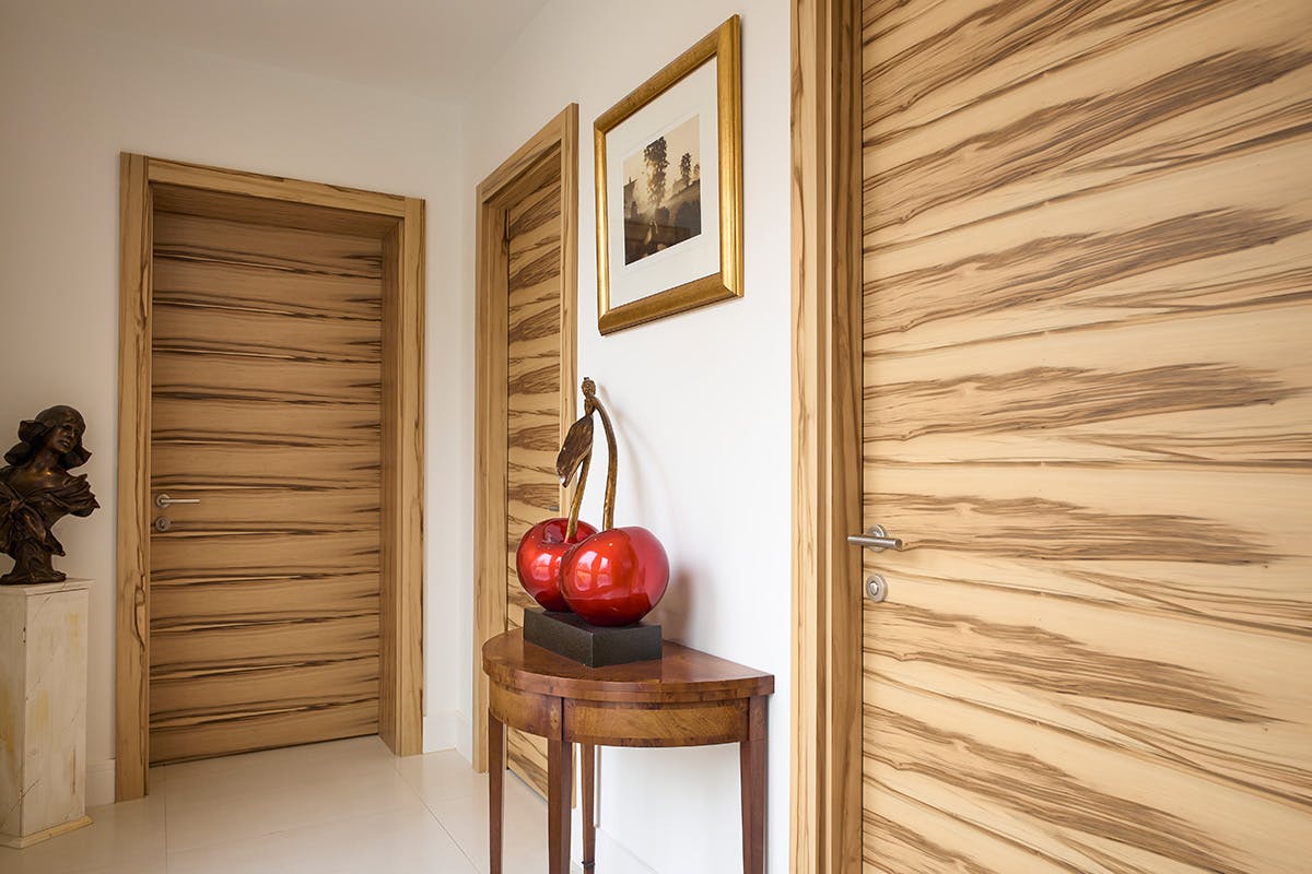 Light flooded hallway with three Deuren pre-hung door sets - Trem H style in Satin walnut finish with lever handles.