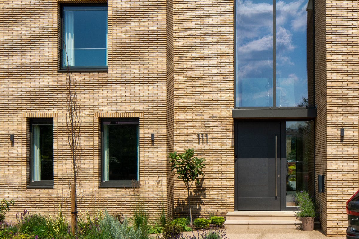 modern home exterior with slim yellow/sand brick, anthricite windows and matching colour bespoke front door by Deuren - Versare style with full height window to the right.