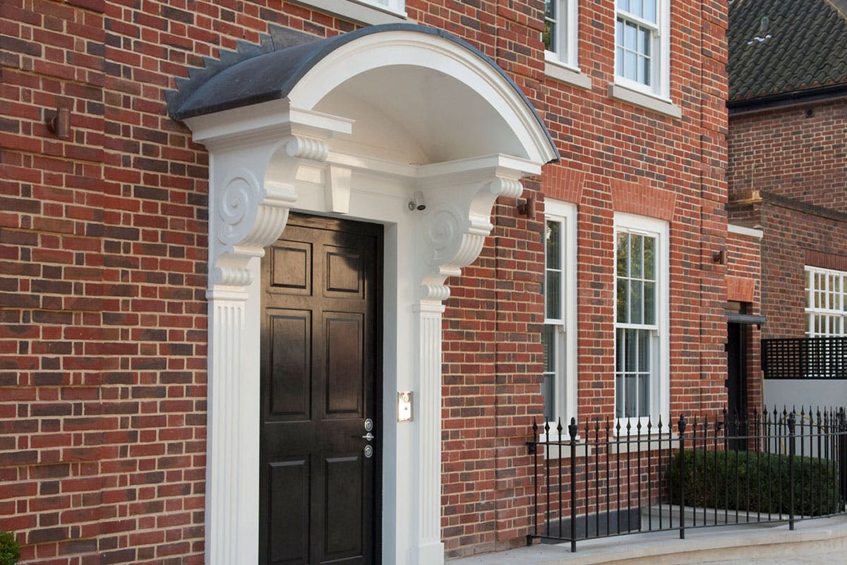 Red brick Georgian style home with arched porch, featuring a classic 6 panel, period style front door in Black paint finish by Deuren