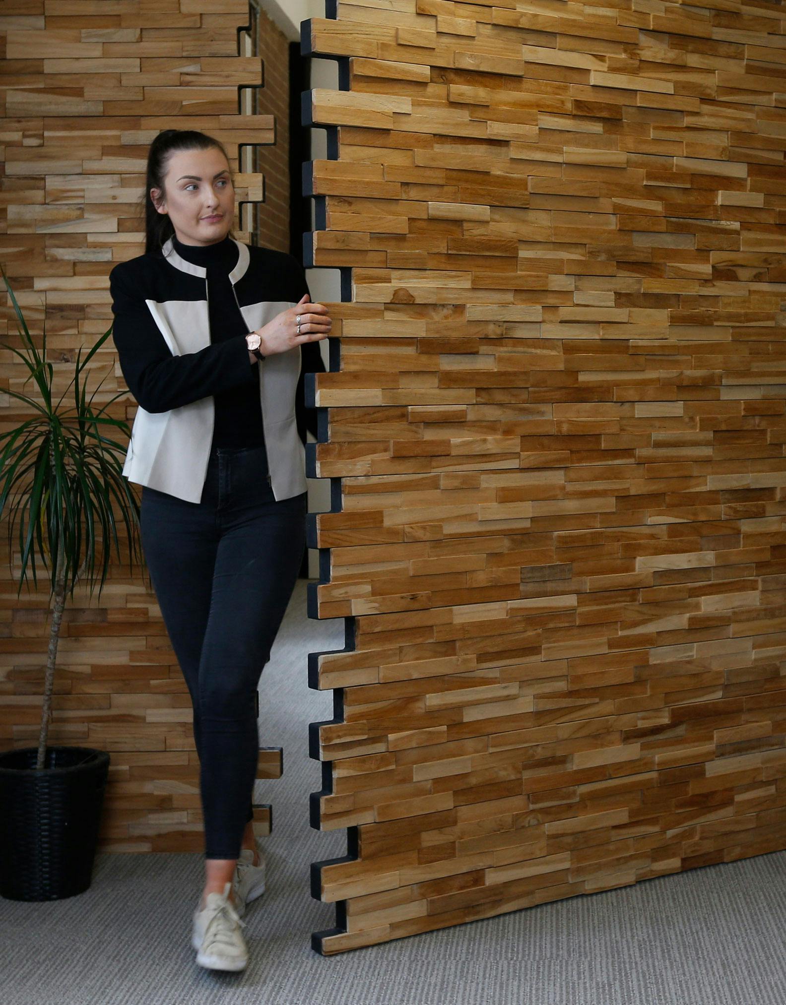 Woman coming through bespoke and contemporary secret pivot door by Deuren. The door and surrounding wall surfaces are finished in stacked timber blocks. A creative door style.