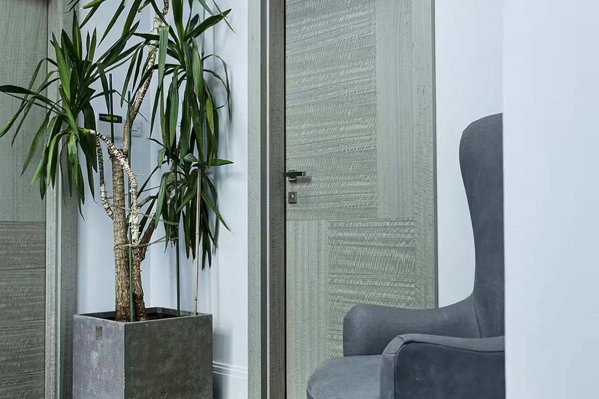Grey interior with contemporoary internal door set - Vario 4 in a grey Eucalyptus finish by Deuren, with tall plant to left and arm chair to the right.