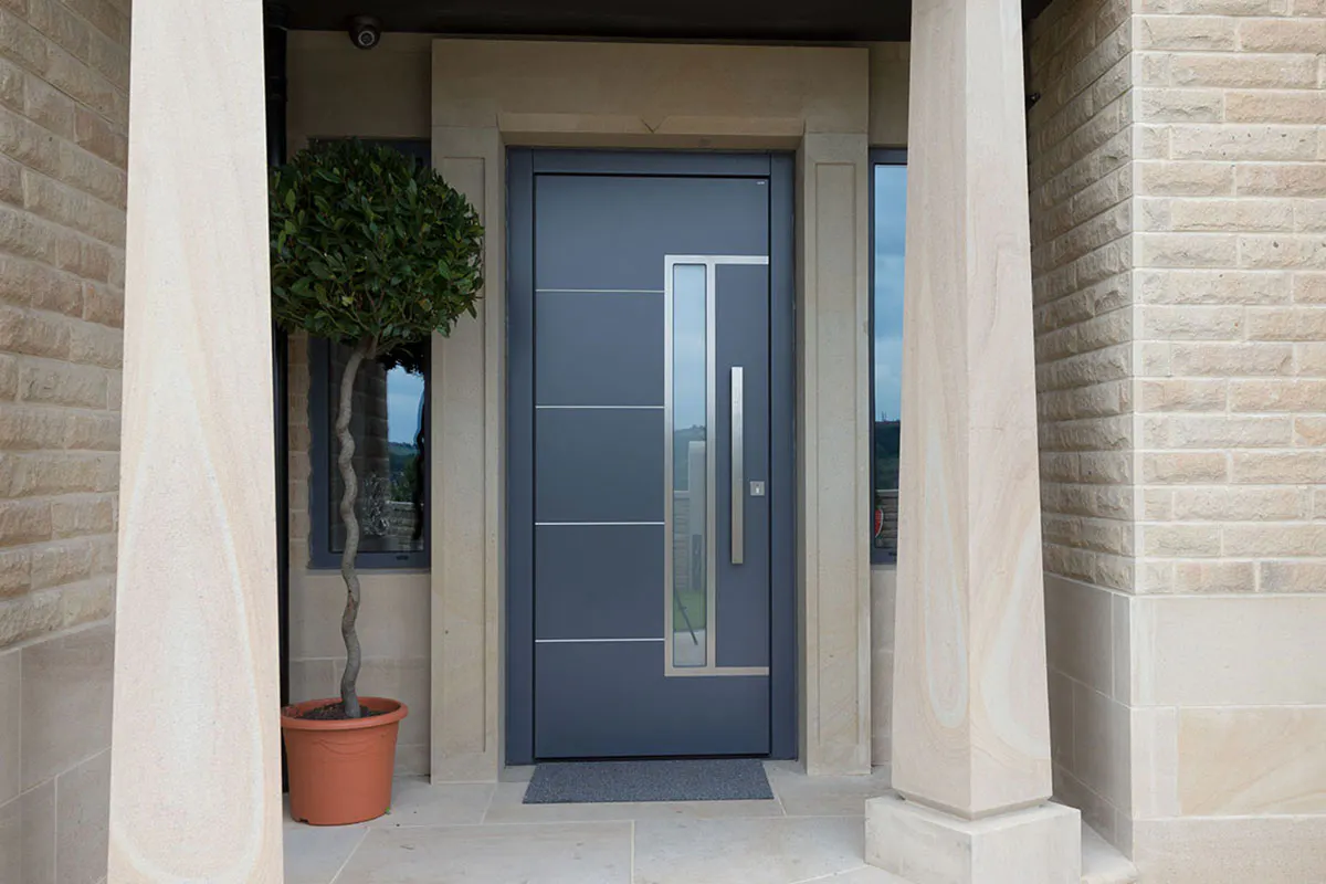 Modern front door by Deuren - Pianura 2 in a smooth, anthricite finish with four evenly spaced, horizontal, stainless steel inlays. It features a long vertical window to the side of a bar handle.