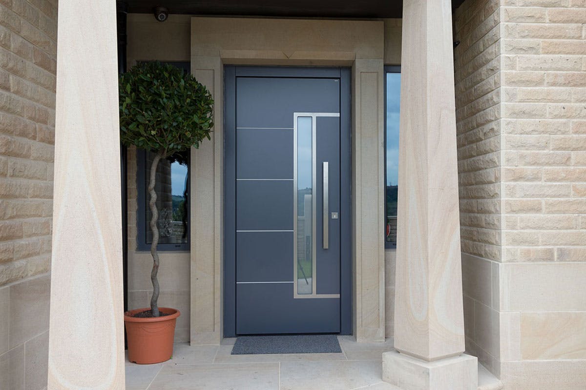 Modern front door by Deuren - Pianura 2 in a smooth, anthricite finish with four evenly spaced, horizontal, stainless steel inlays. It features a long vertical window to the side of a bar handle.