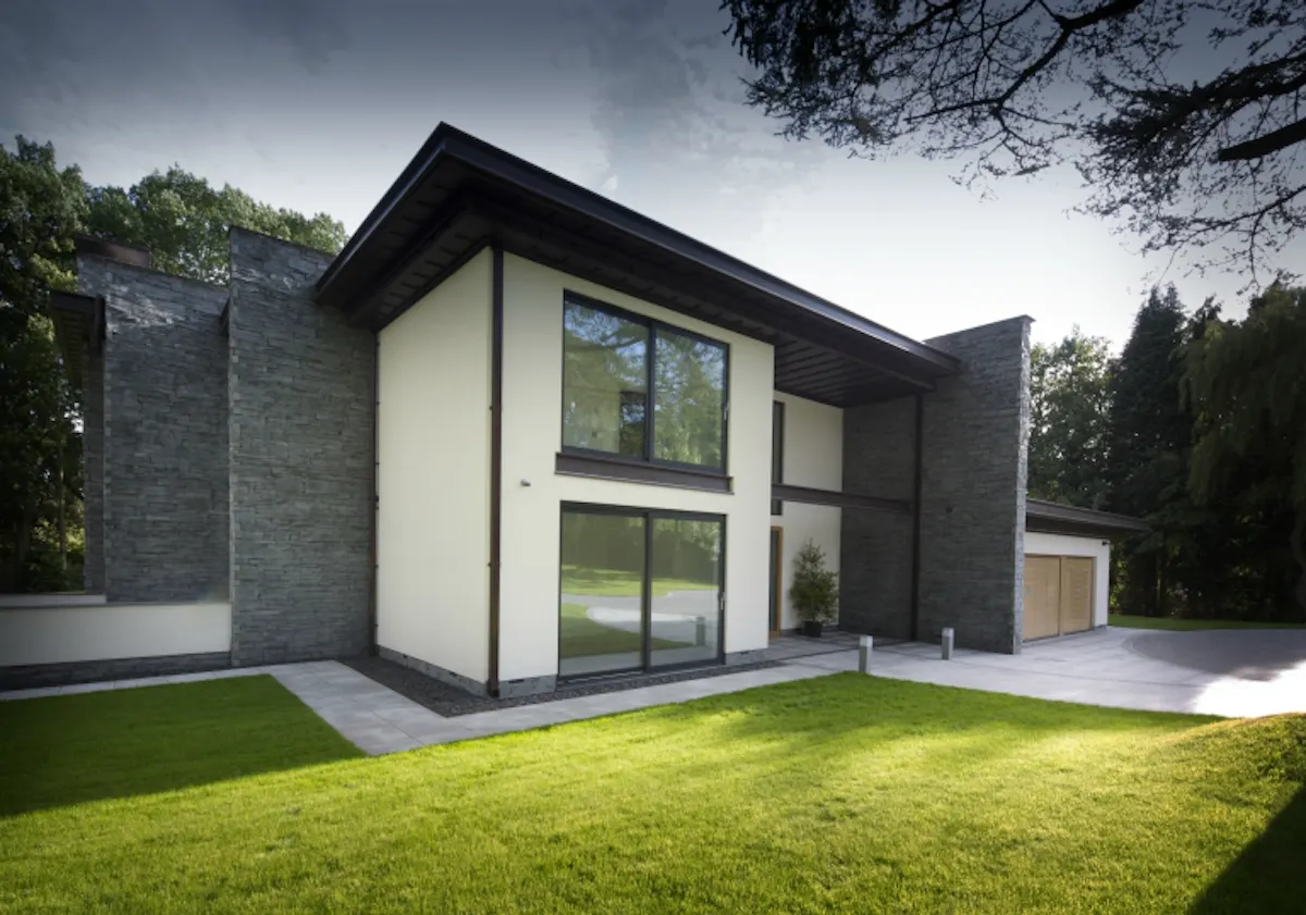 Large modern home featuring a mix of slate, whiite render and large black framed windows, featuring natural oak garage door by Deuren
