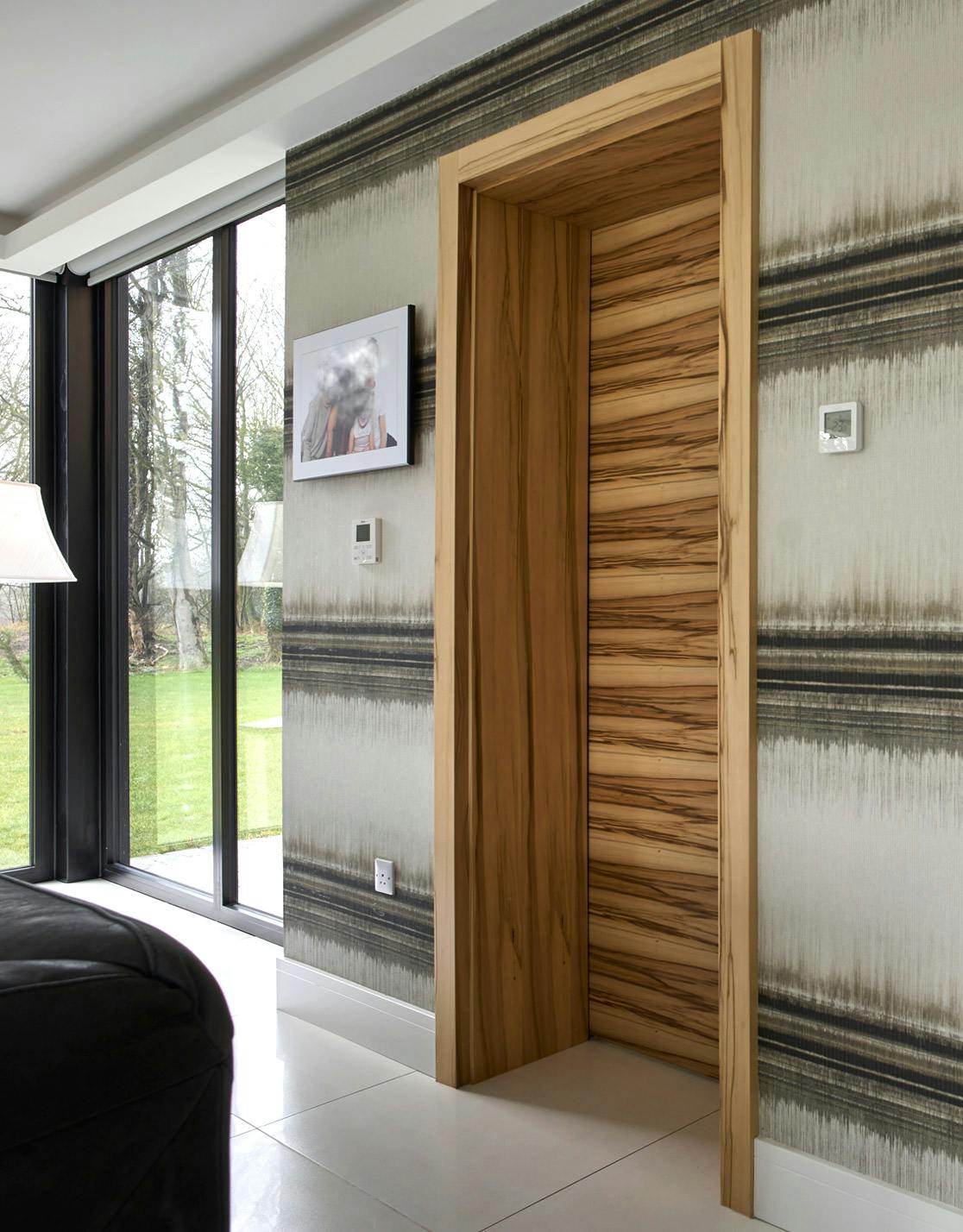 Modern lounge with a made-to-measure pre-hung door set from Deuren - Trem H style in Satin walnut finish with lever handles. Demonstrates Deuren's capability to make deep door frames.