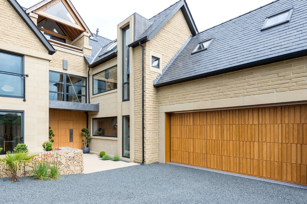 Wide view of Yorkshire stone home exterior with a bespoke matching front and garage door by Deuren - Tavole in Honey Oak